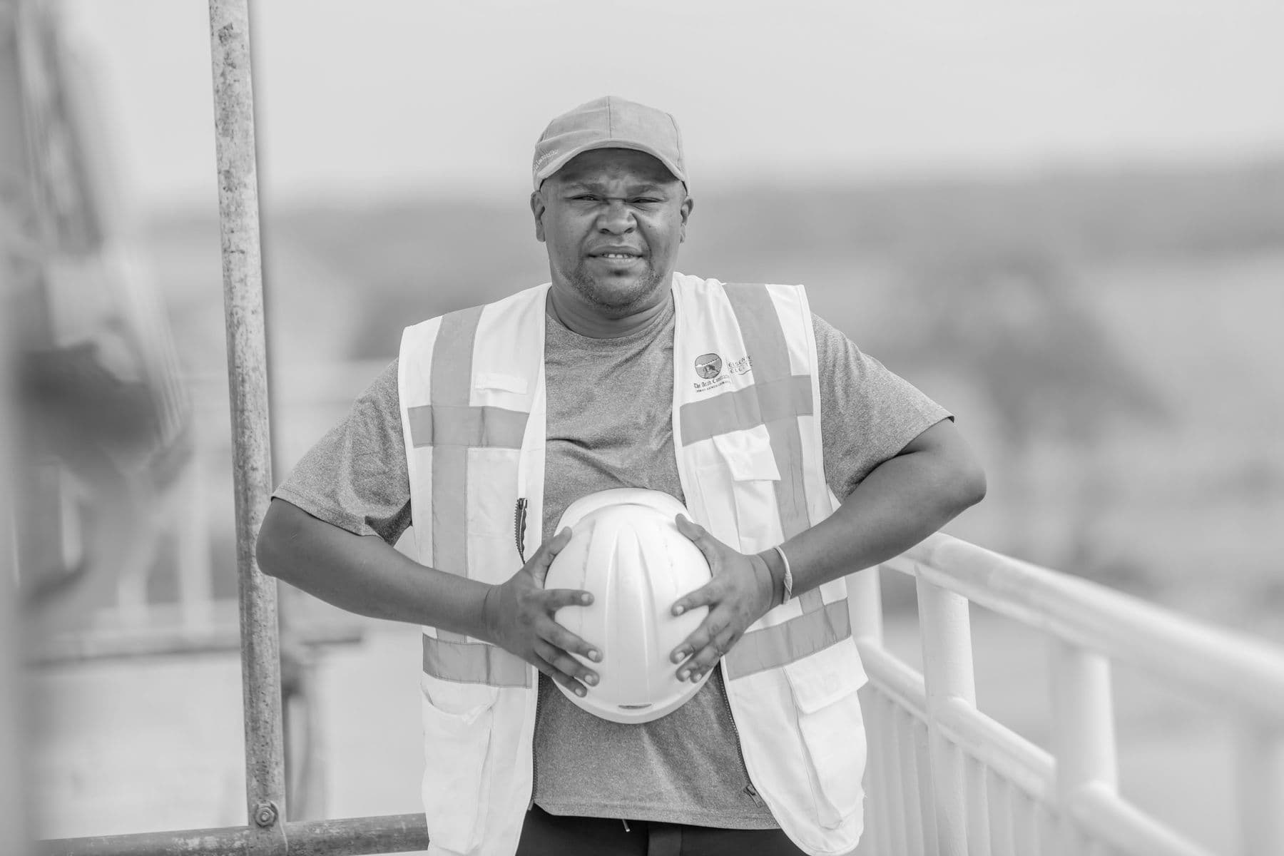 Black and white photo of a construction worker holding a helmet outdoors.