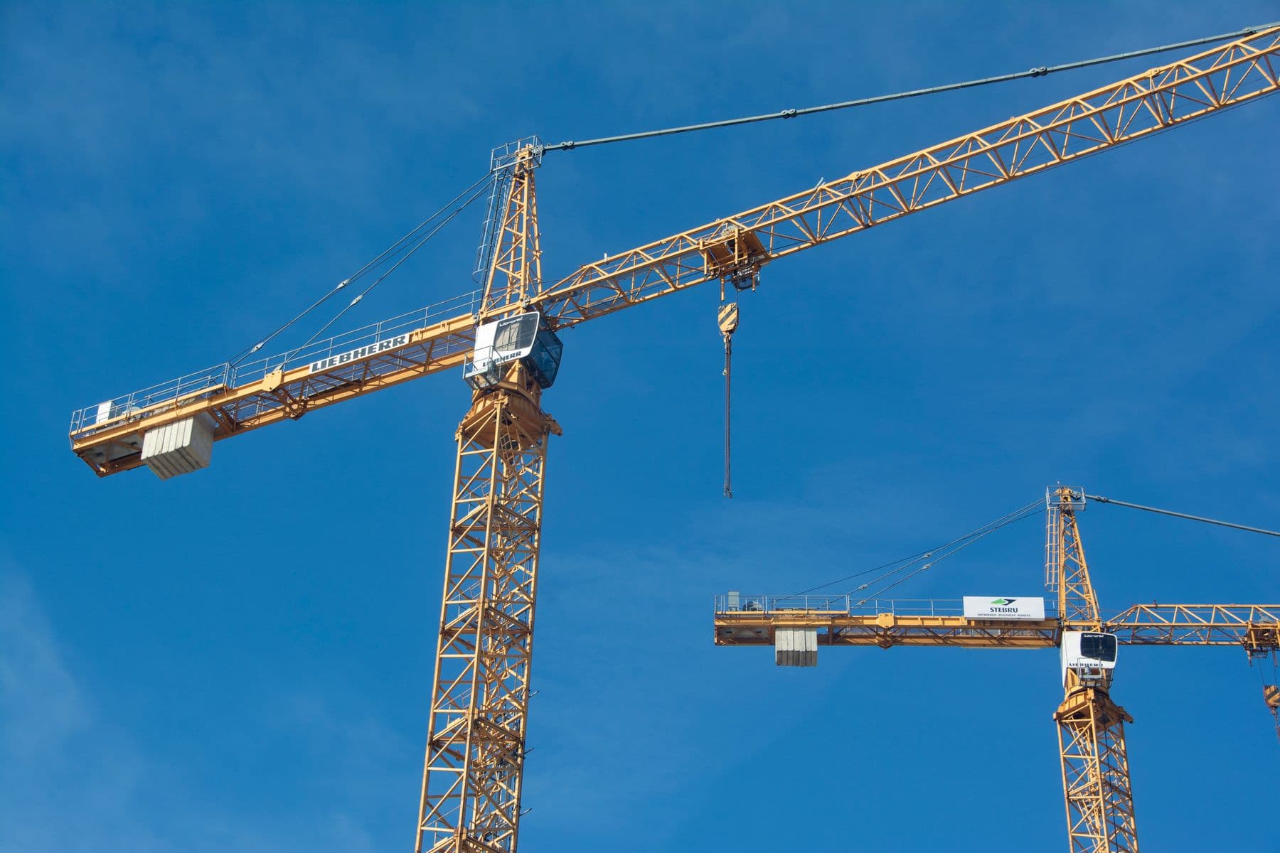 Tower cranes soar high against a bright blue sky, showcasing powerful construction equipment.