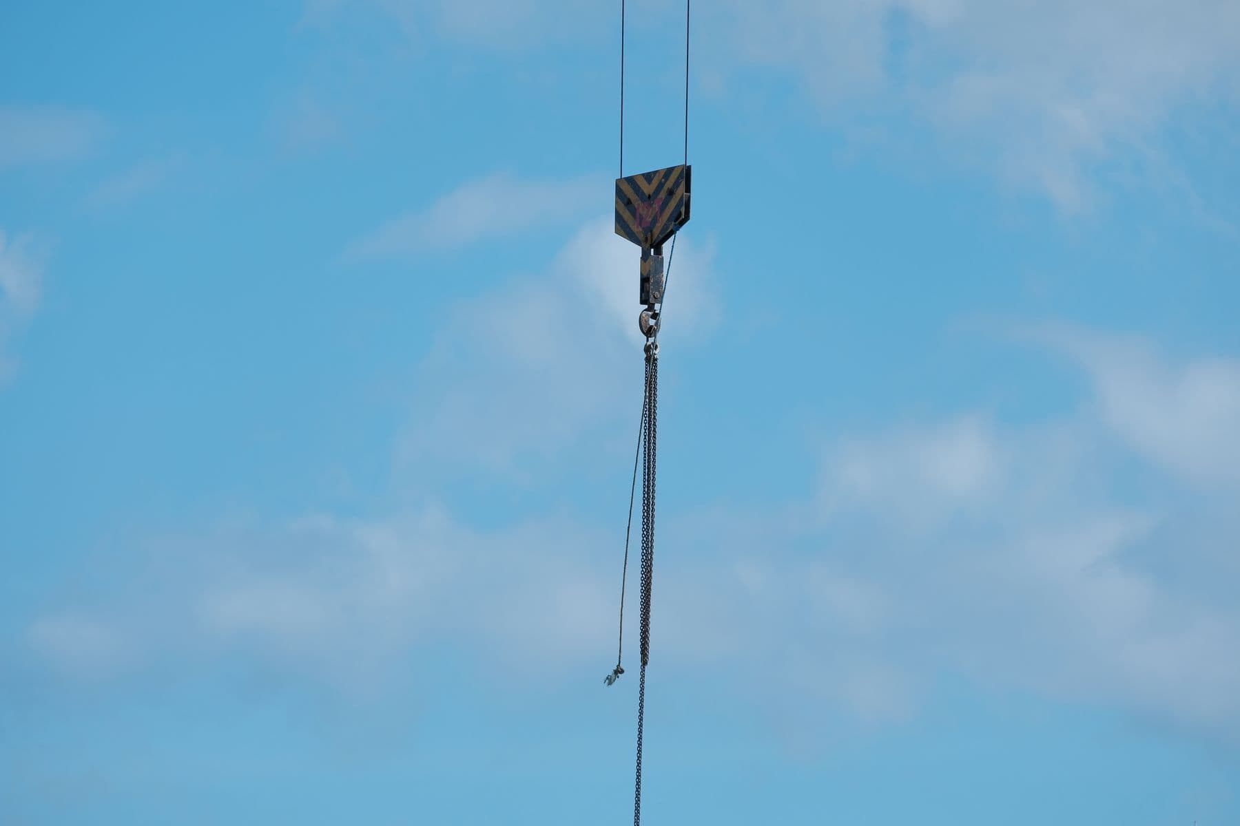 A detailed view of a crane hook suspended against a bright blue sky, illustrating industrial themes.