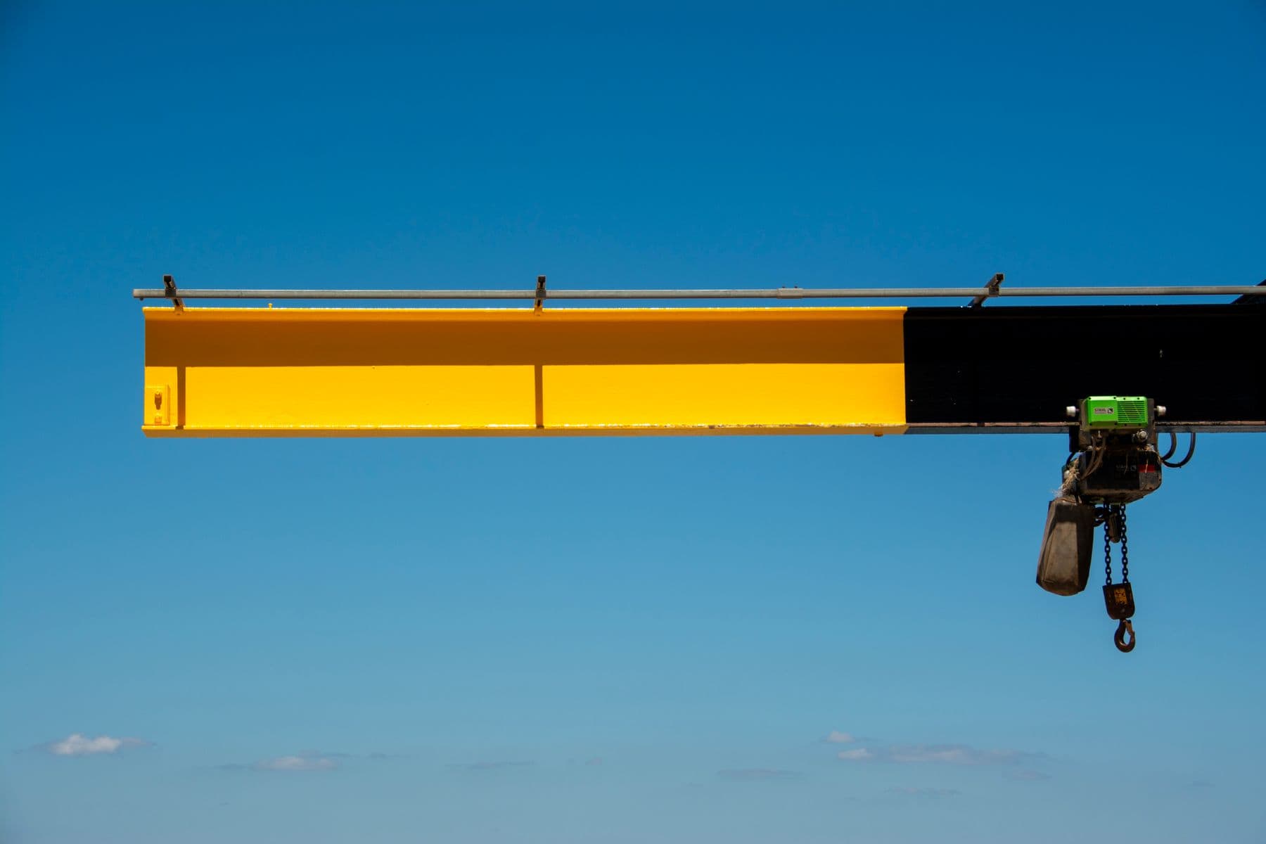 Bright yellow crane arm extending against a clear blue sky, ideal for industrial themes.